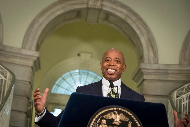 Mayor Eric Adams smiling behind a lectern in New York City Hall