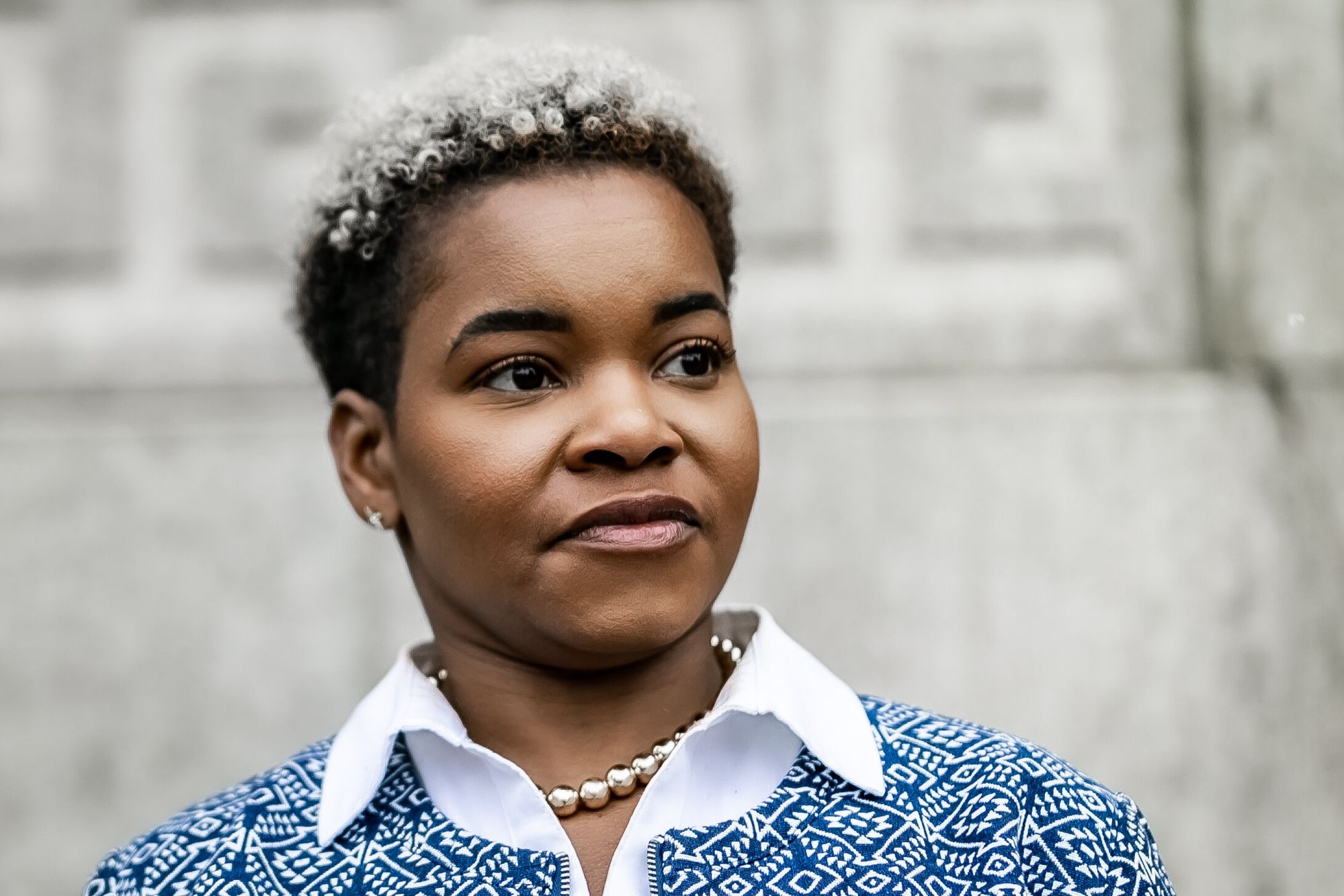 India Walton standing in patterned jacket before a stone wall