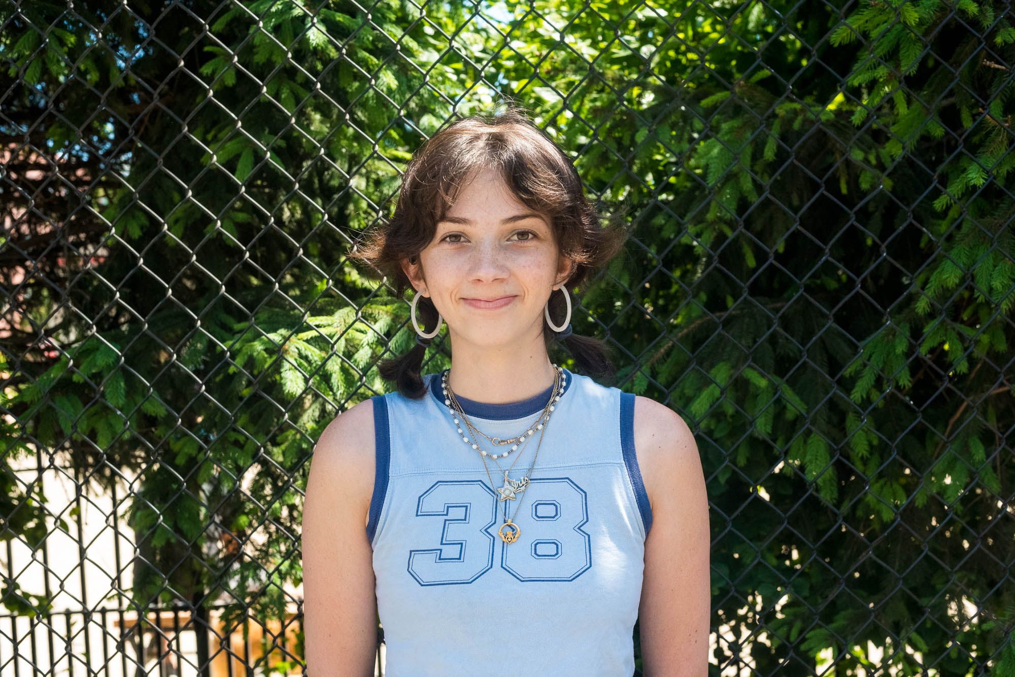 Erwin wearing a light blue tank with the number 38 on it, white hoop earrings, and several necklaces. 