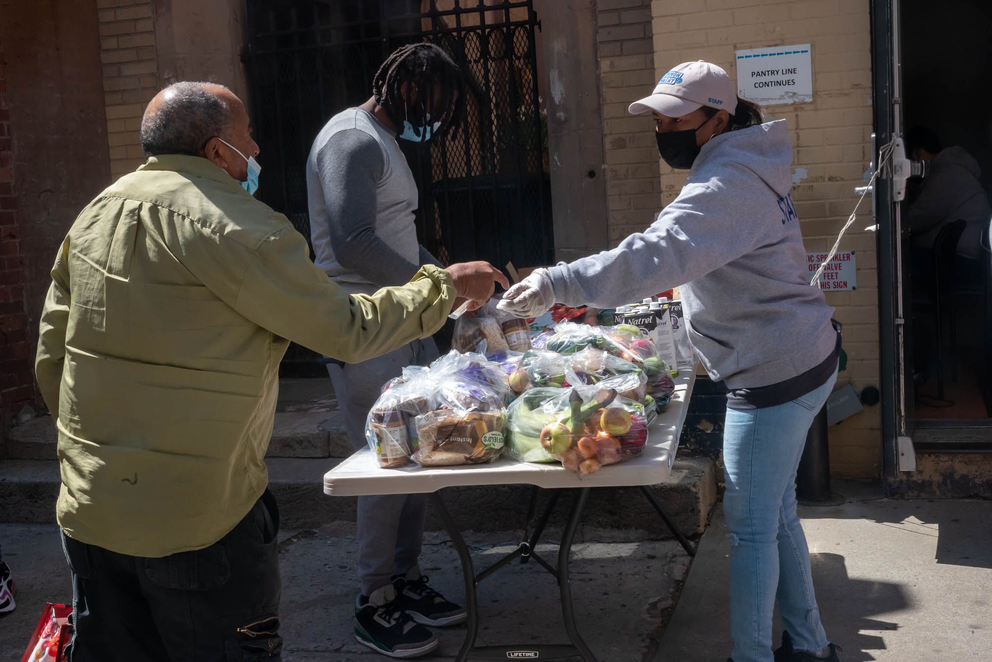 Pantry workers distribute food at a table outdoors.