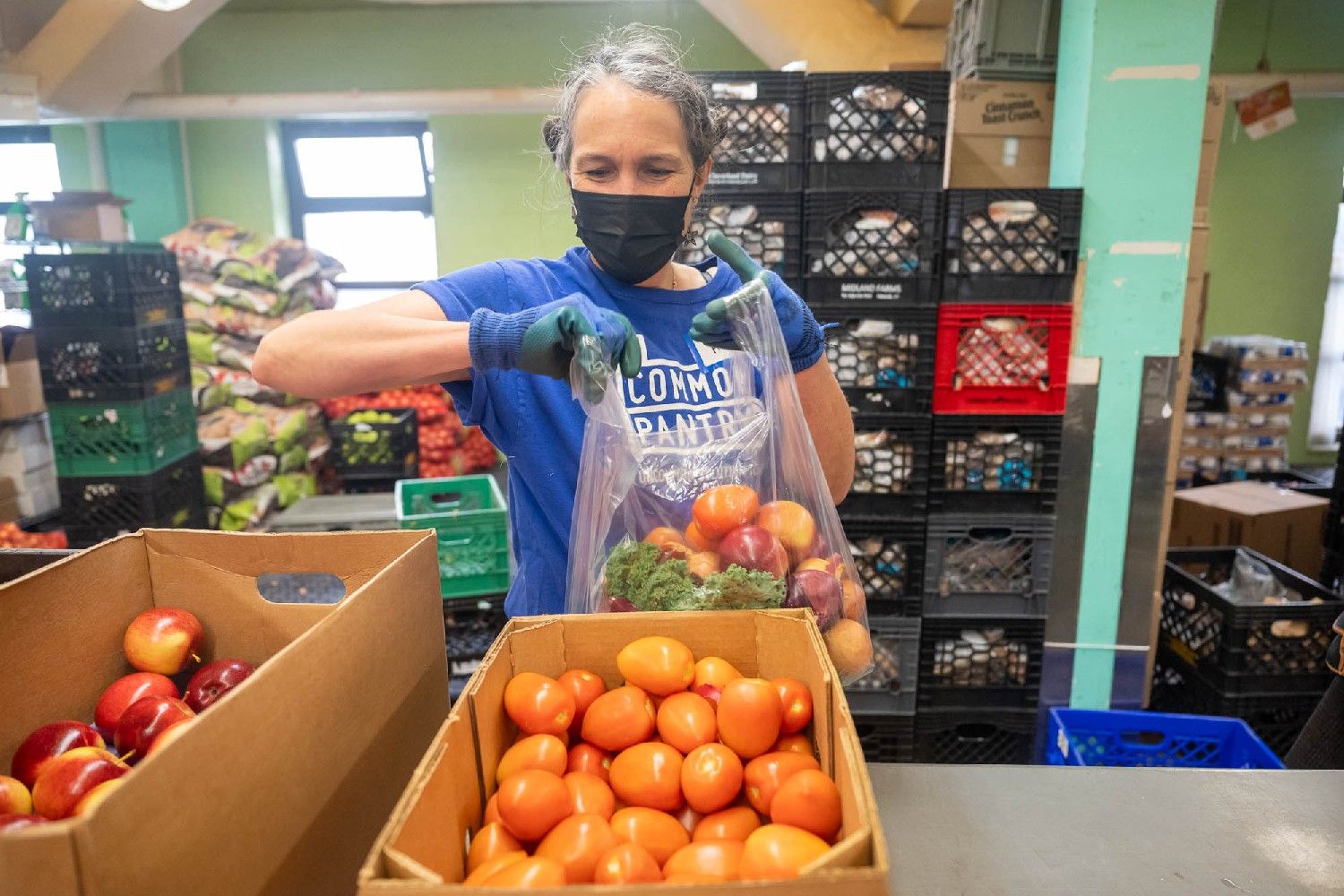 A worker fills a plastic bag with produce.