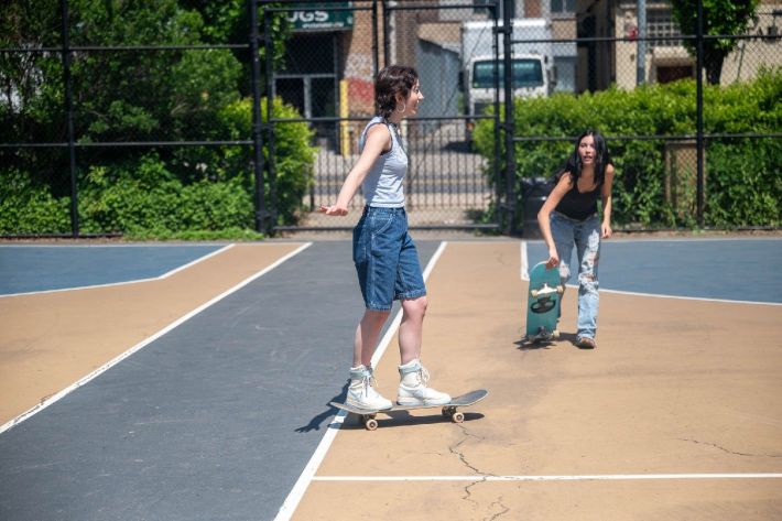 Erwin floats on their board, wearing high-top white sneakers and long blue jean shorts. Bryan is about to hop on her board in the background.