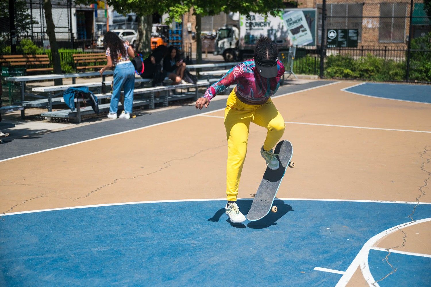 Vasquez skating with her board mid-air. She's wearing a bright-color pink and blue top with yellow pants.