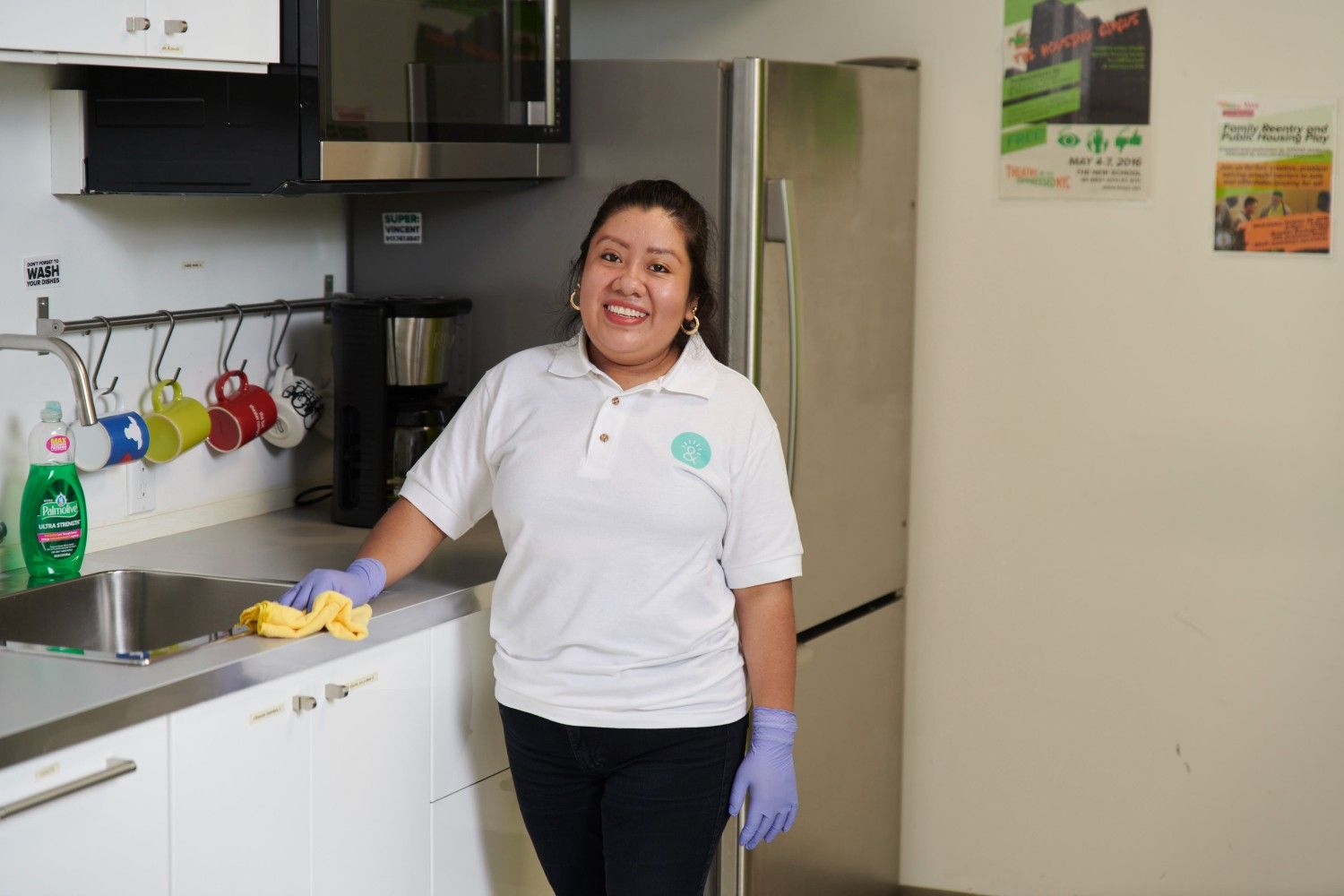 Aguilar stands in a kitchen facing the camera with cleaning gloves on.