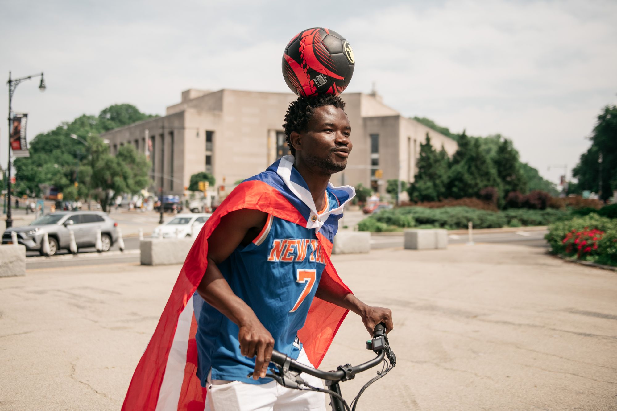 Leh-Boy rides a bike while balancing a soccer ball on his head.