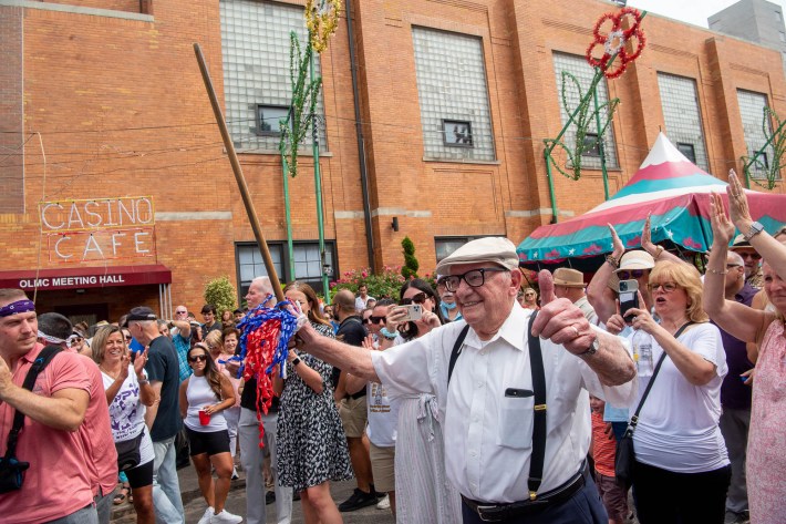 A man in glasses smiles and waves a cane.