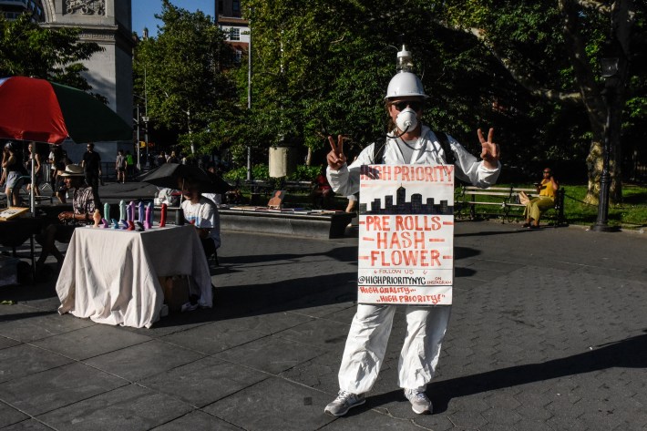 J.P., in an all white jumper and homemade sandwich board advertising pre-rolls, flower, and hash.