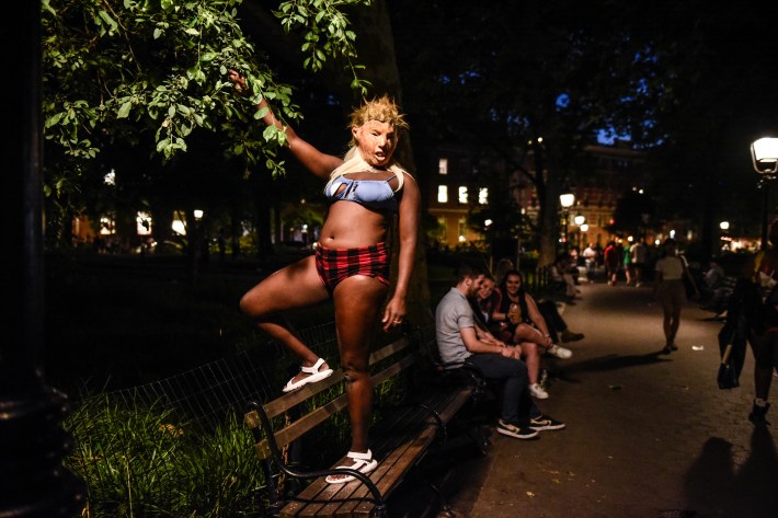 After sunset, a person stands on a bench with a Donald Trump mask.