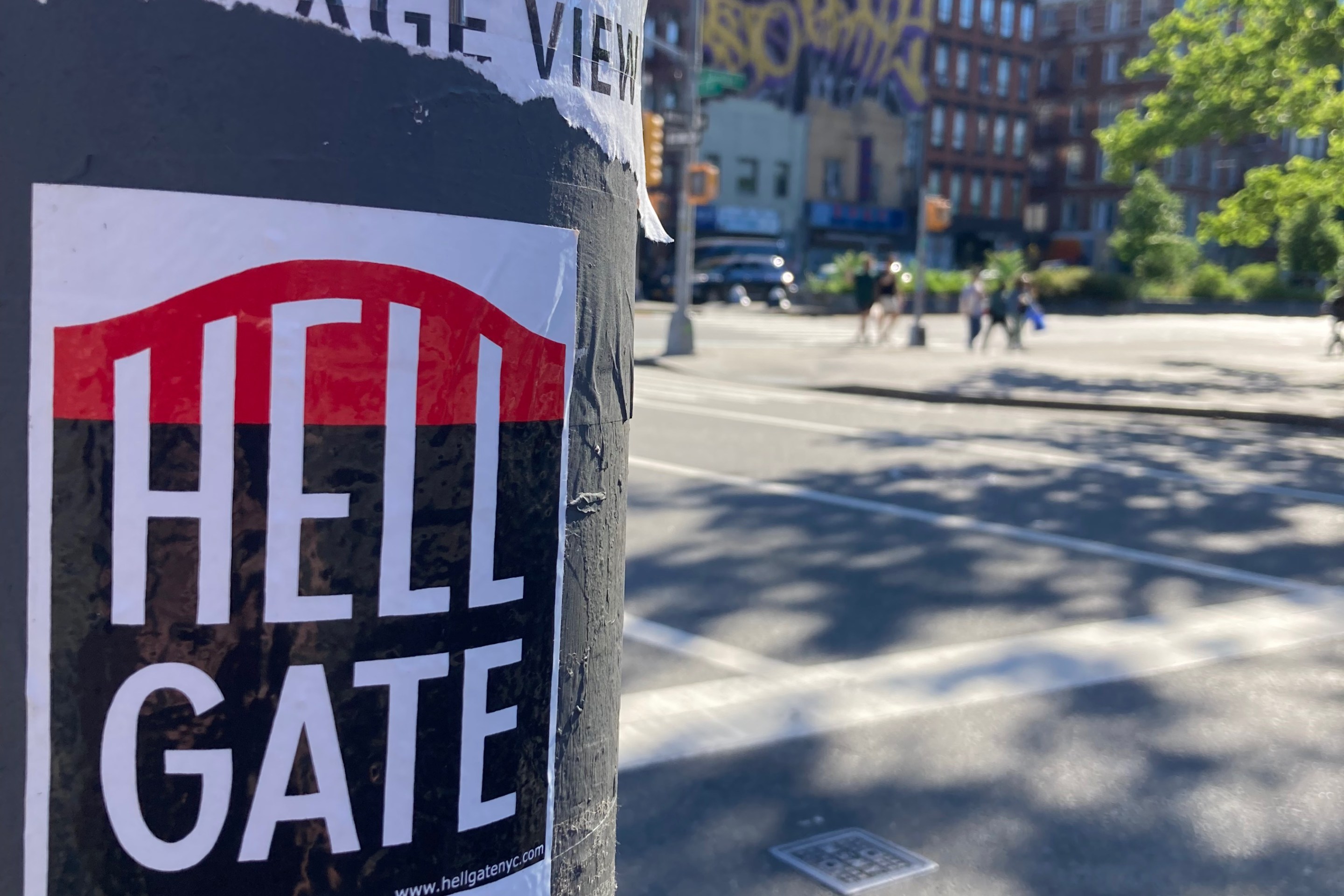 A Hell Gate Sticker on a lamppost in front of a sun-dappled city playground