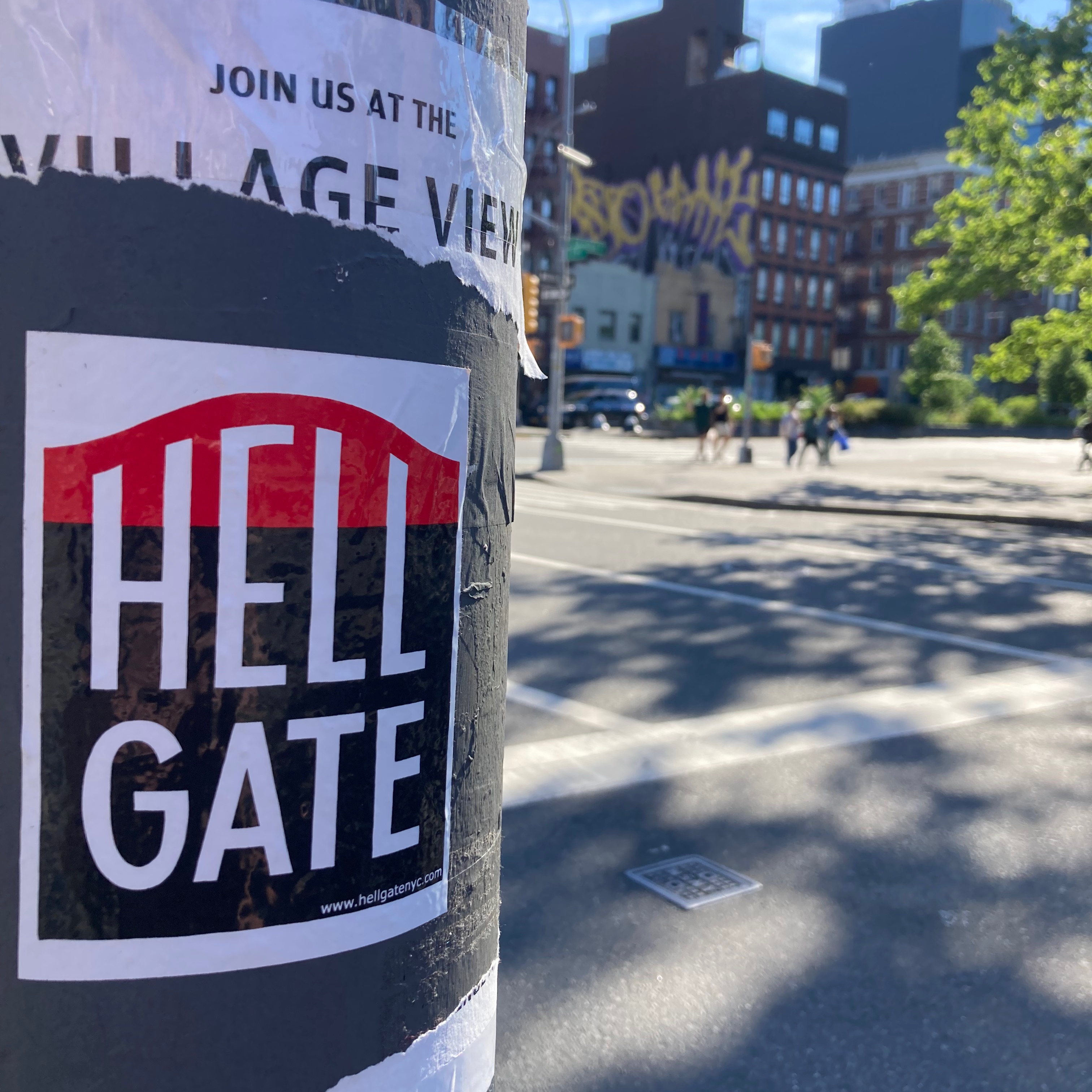 A Hell Gate Sticker on a lamppost in front of a sun-dappled city playground