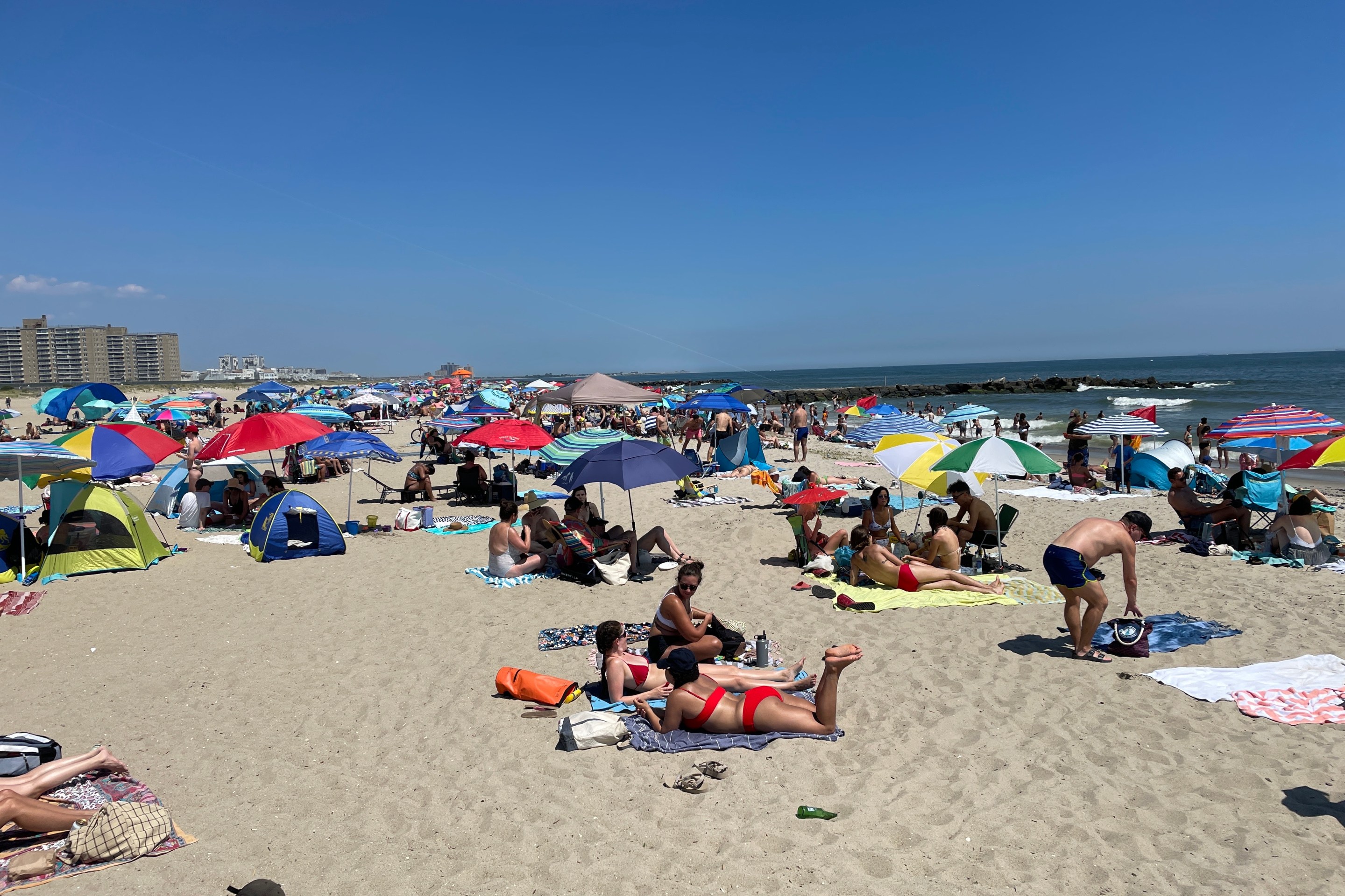 Hundreds of beachgoers sit on blankets on a brilliant summer day in the Rockaways.