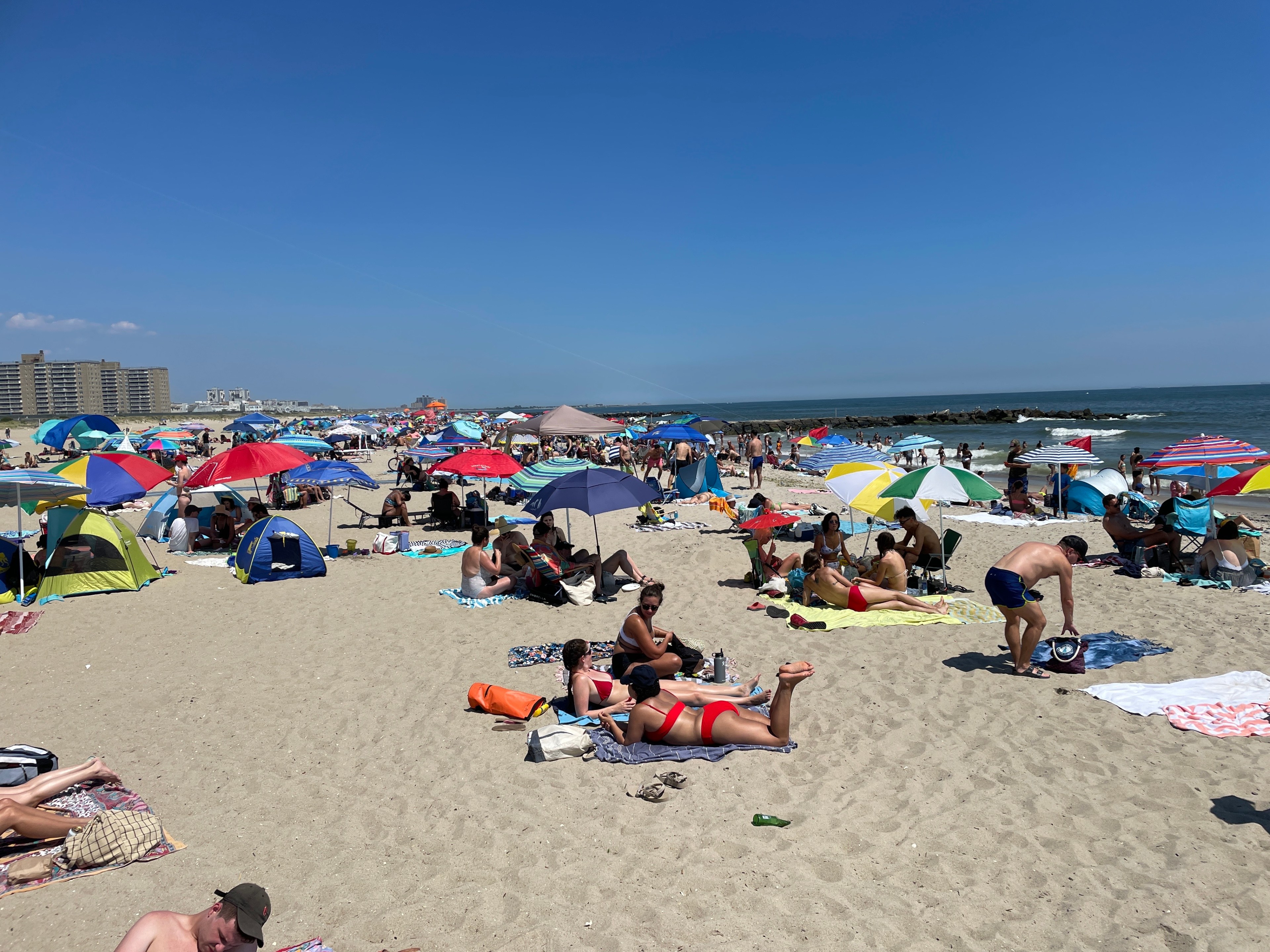 Hundreds of beachgoers sit on blankets on a brilliant summer day in the Rockaways.