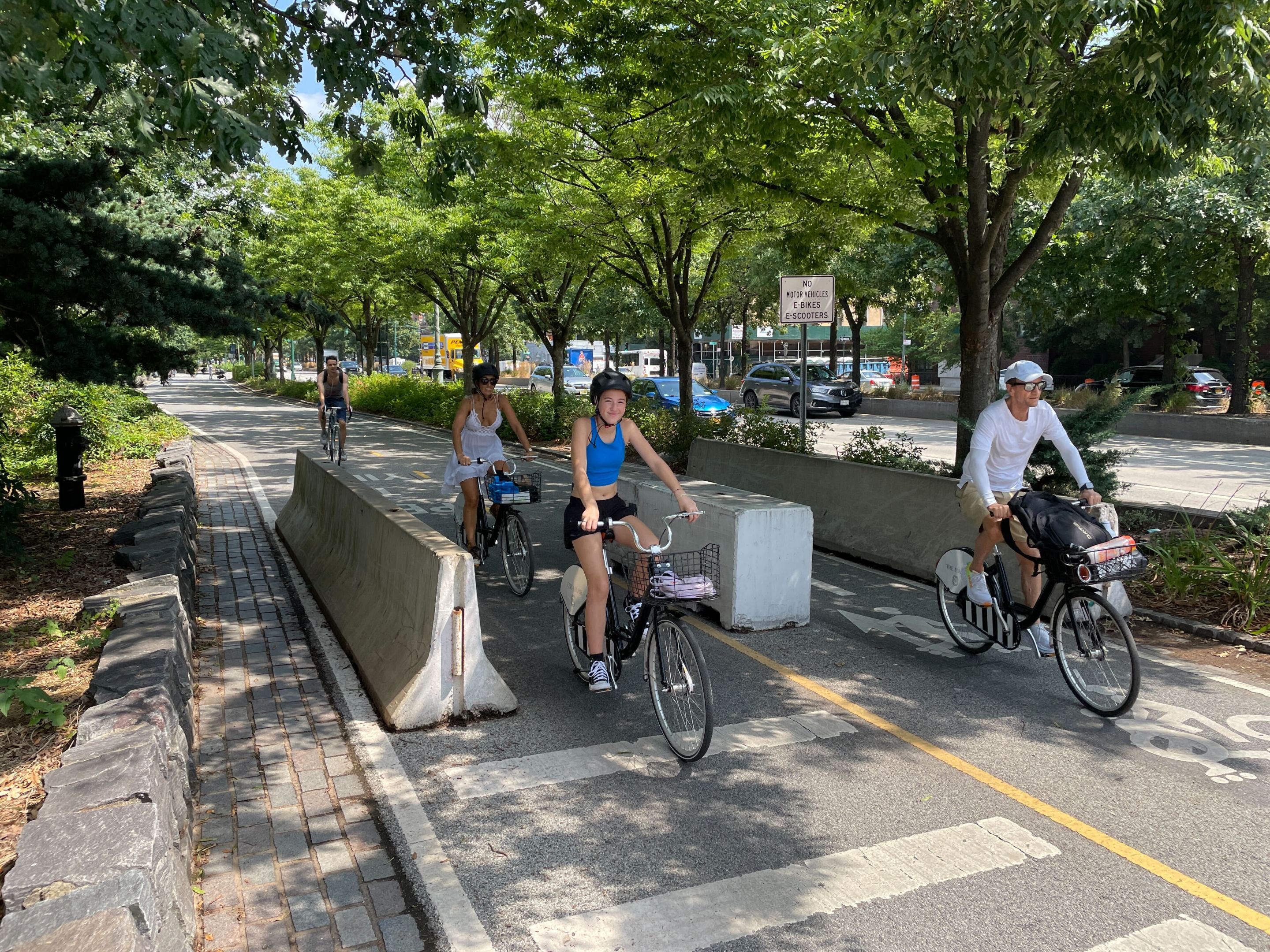 A group of cyclists bike through concrete bollards on the crowded Hudson River Greenway.