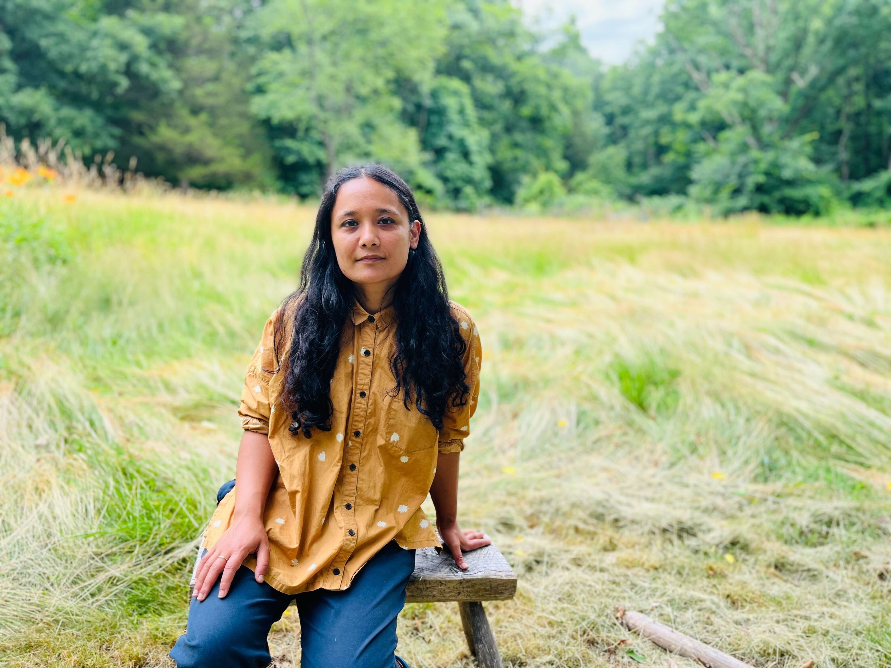 Sarahana Shrestha, the Democratic nominee for NY state Assembly District 103 in the Hudson River Valley, sits on a stool in a grassy field.