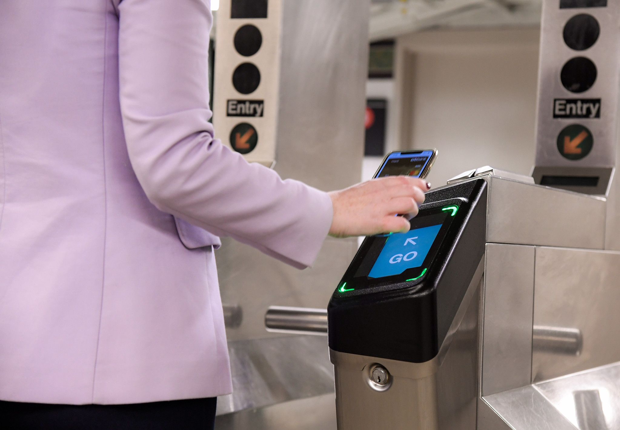 A person taps their smart phone on an OMNY reader to enter the subway system.