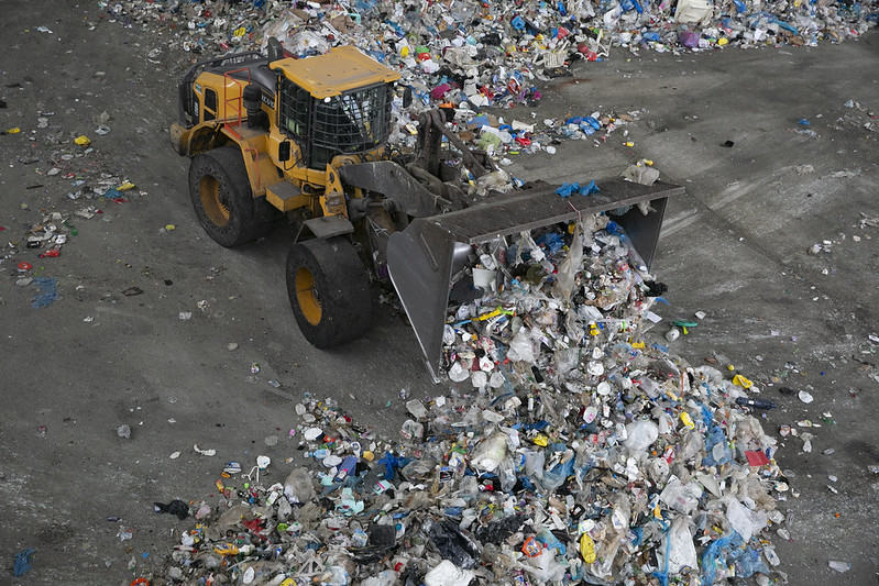 A yellow truck pushes a mound of recylables.