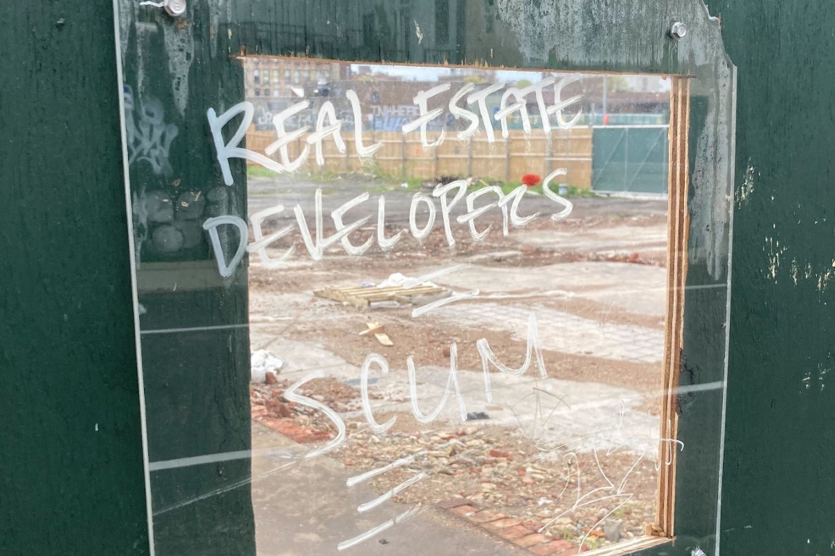 A message reading "real estate developers = scum" written in white on a sheet of plexiglass.