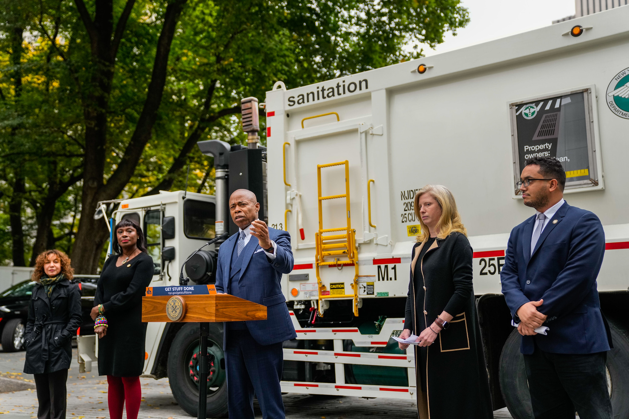 Mayor Eric Adams, DSNY Sanitation Commissioner Jessica Tisch, and others stand in front of a DSNY truck to announce a new rule that would require New Yorkers to set their trash out no earlier than 8 p.m.