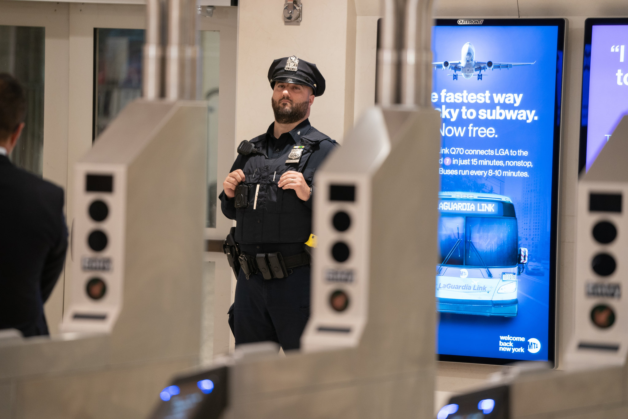 An NYPD officer stands watch outside a subway turnstile.