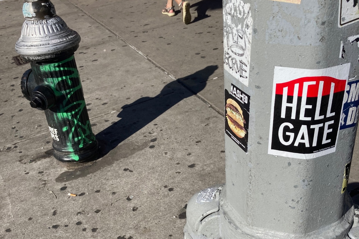 A Hell Gate sticker on a lamppost, next to a fire hydrant.
