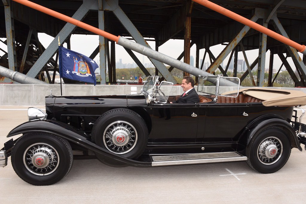 Former Governor Cuomo Announces the Opening of the First Span of the Kosciuszko Bridge in New York City by driving over it in an old timey car driven by FDR.
