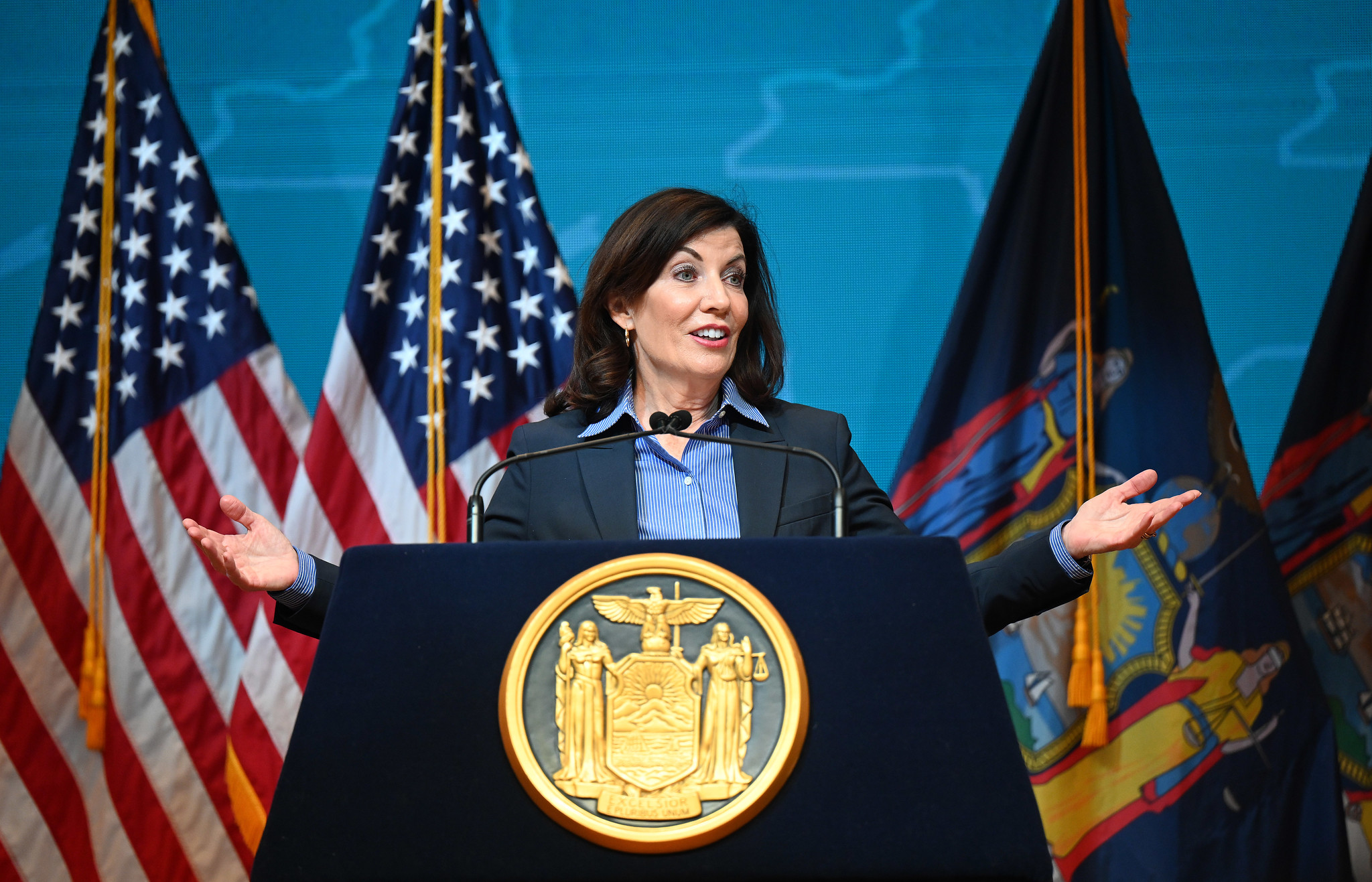 Governor Kathy Hochul speaks at a podium with her arms outstretched.