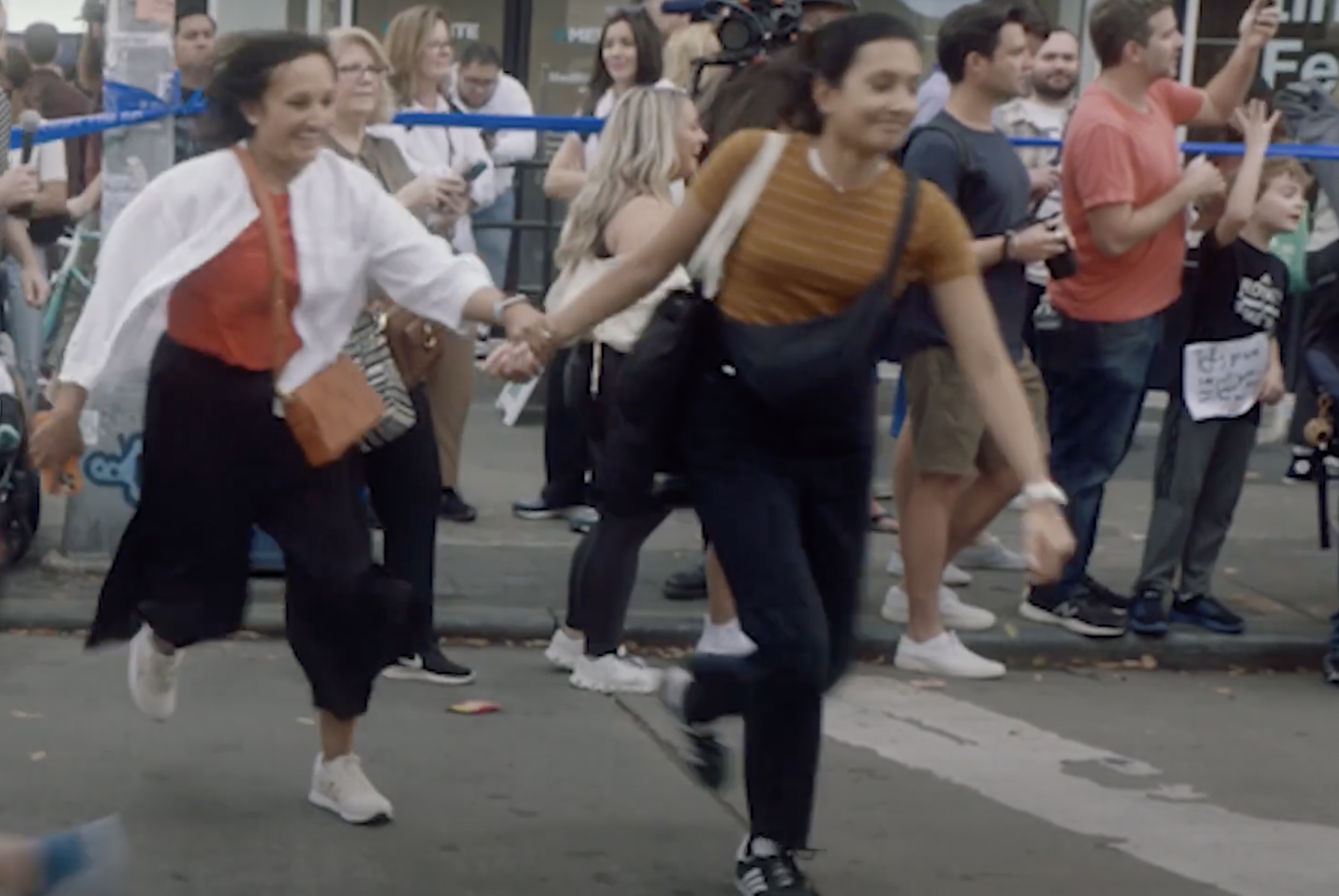 Two women hold hands and cross the NYC Marathon laughing.