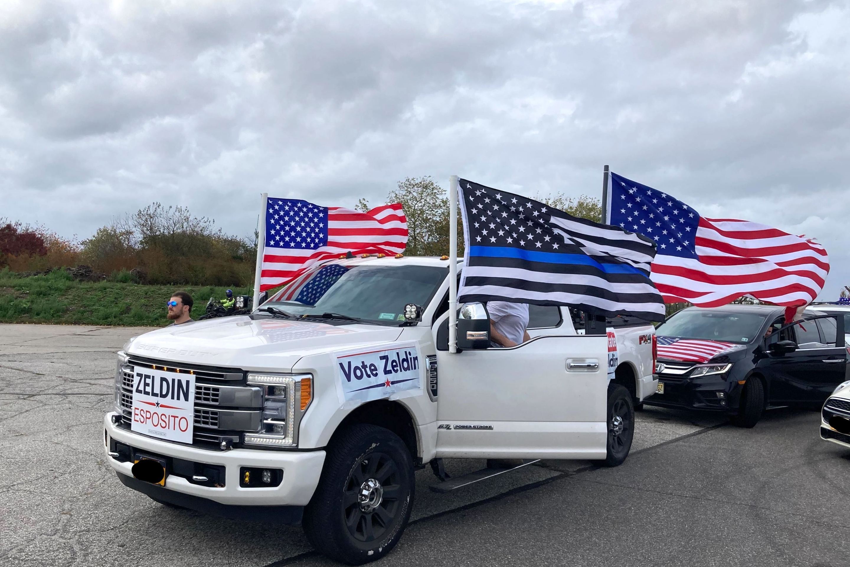 A huge white Ford pickup truck sporting American flags and Thin Blue Line flags and Lee Zeldin posters.
