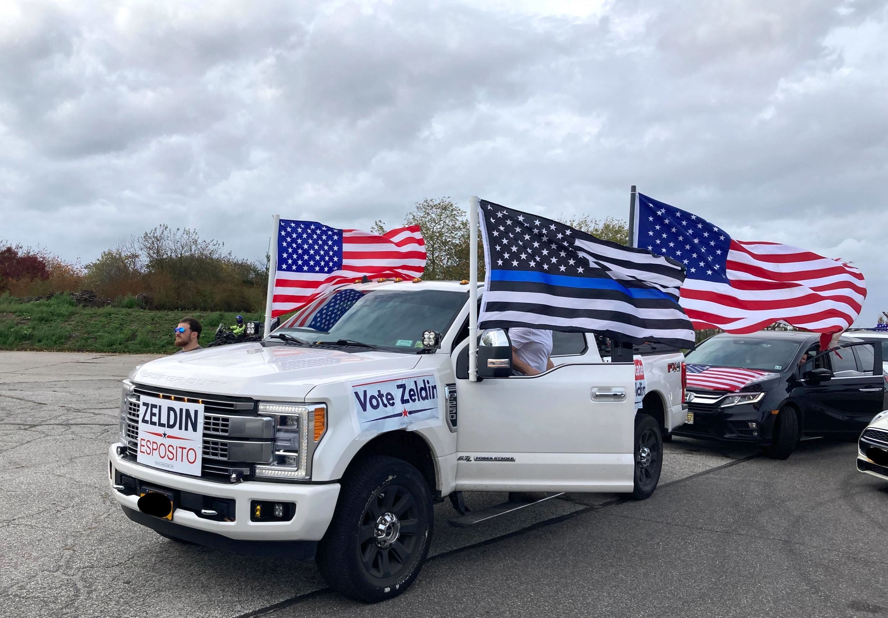 A huge white Ford pickup truck sporting American flags and Thin Blue Line flags and Lee Zeldin posters.