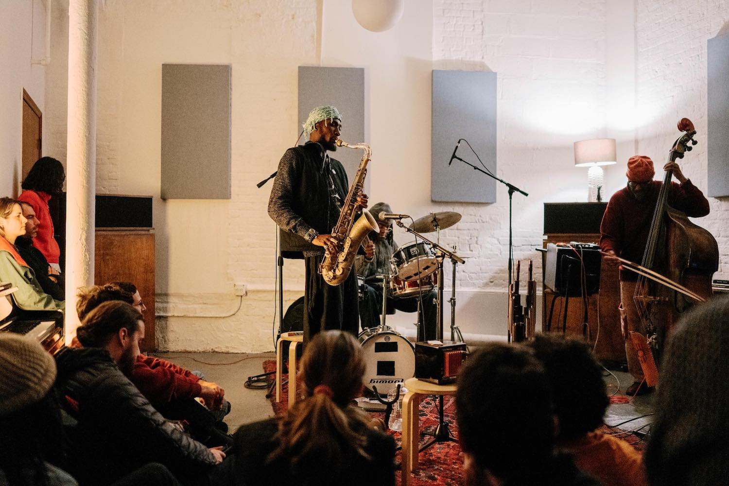 A group of musicians perform at Blank Forms while audience members sit on a carpet and watch.