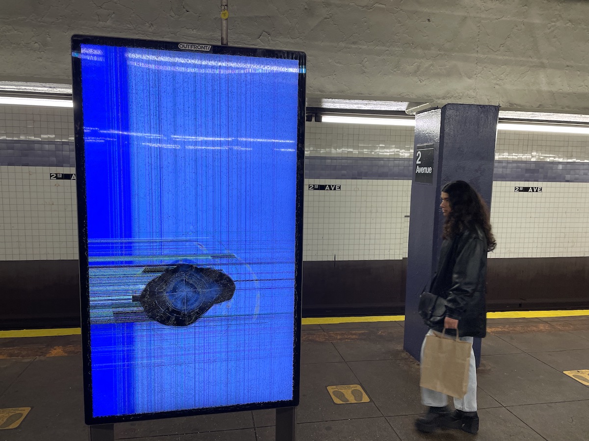 An MTA information screen has been punched out and displays glitches on the subway platform.