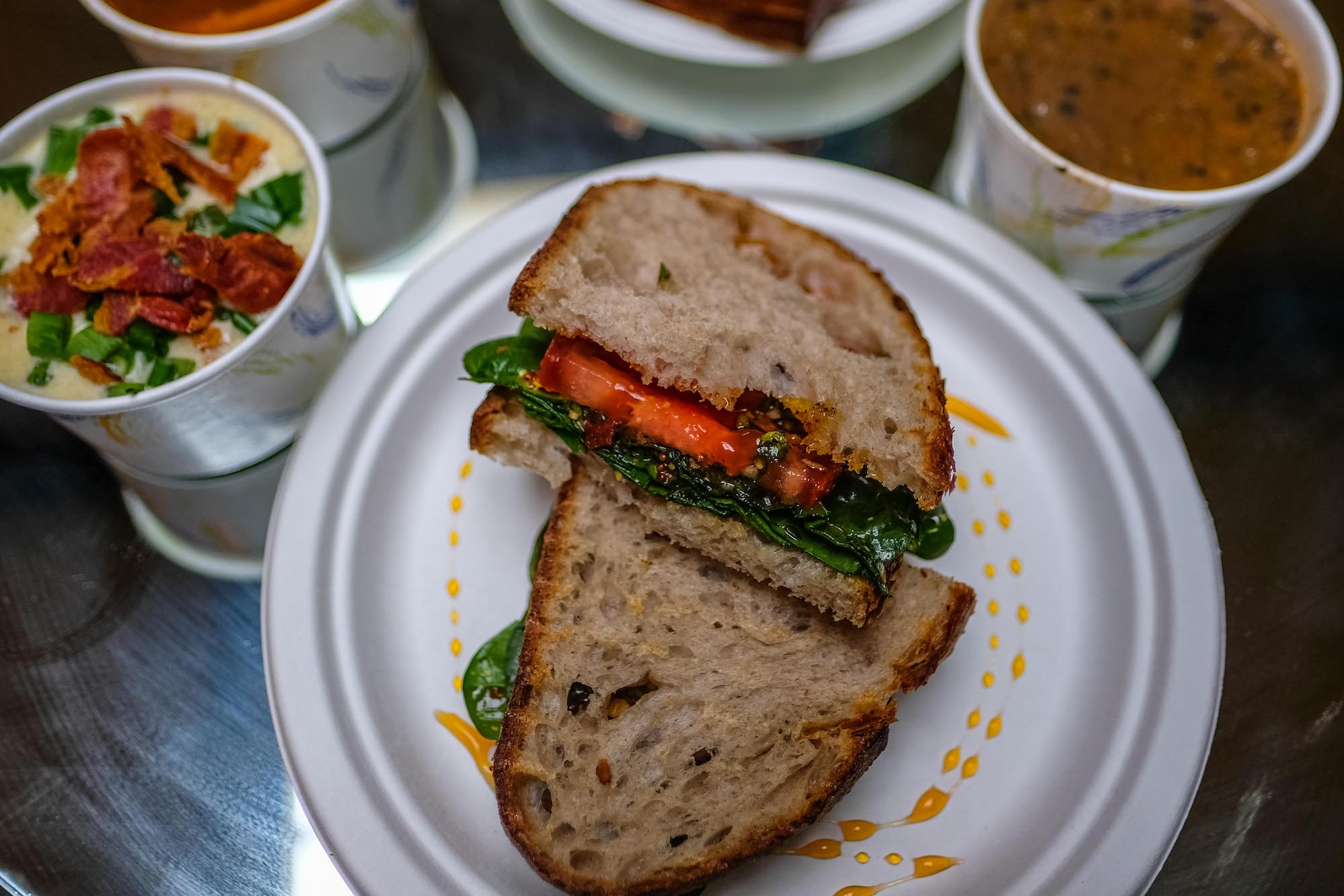 A vegan sandwich called The Gunther sits on a plate surrounded by various soups.
