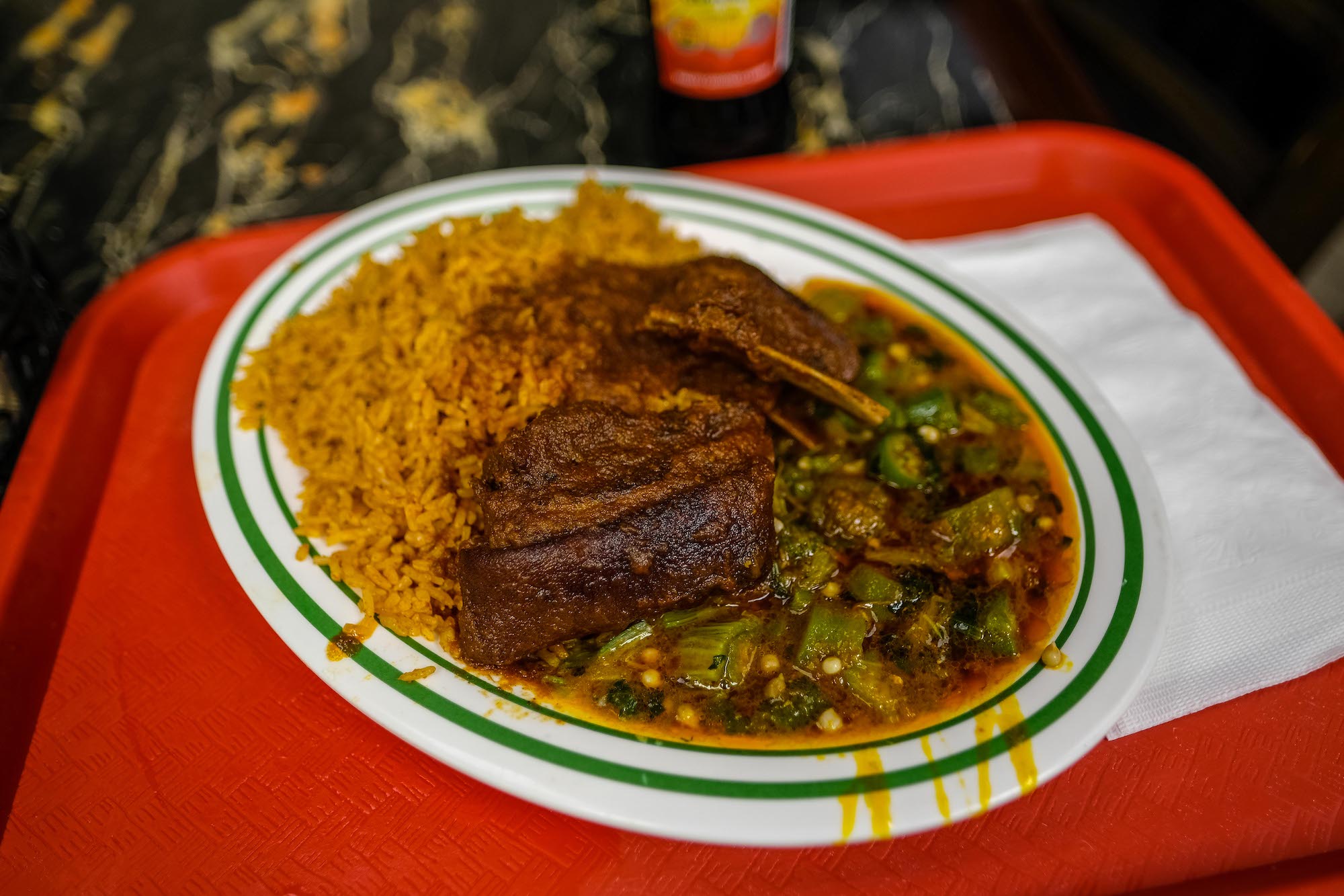 A plate of goat, with jollof and okra, on a red tray.