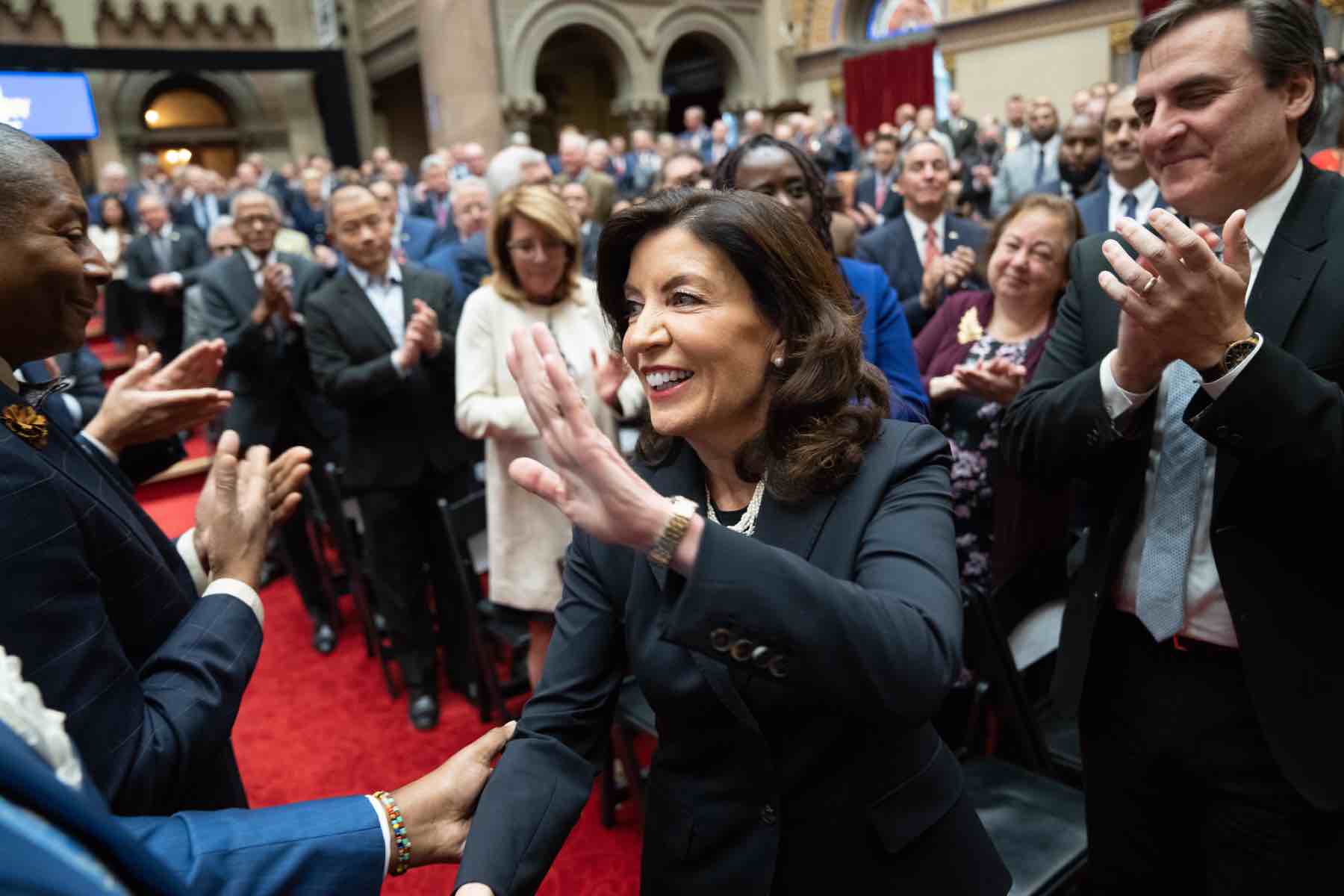 Governor Hochul surrounded by applauding lawmakers.