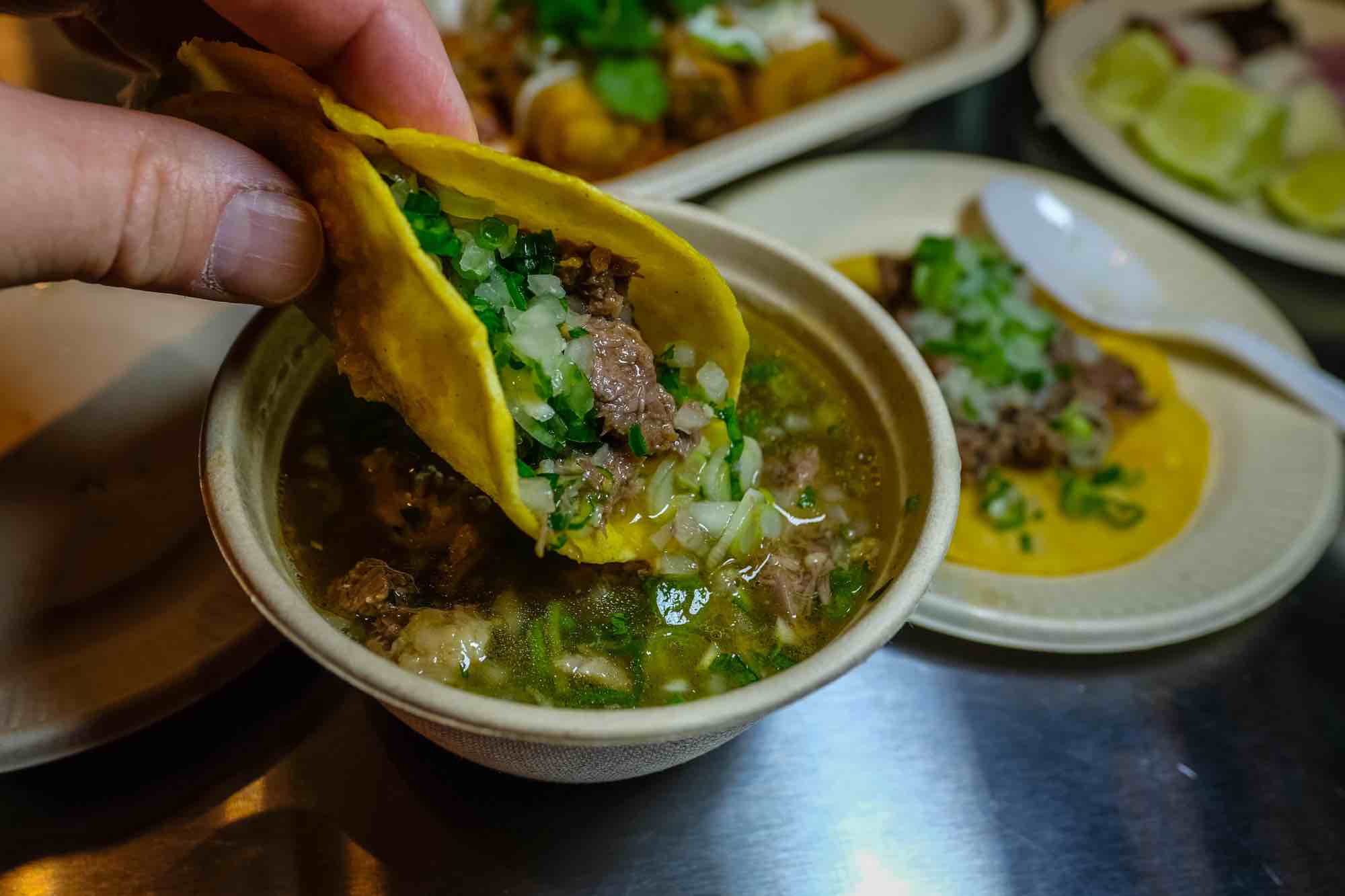 A taco being dipped into delicious consome.