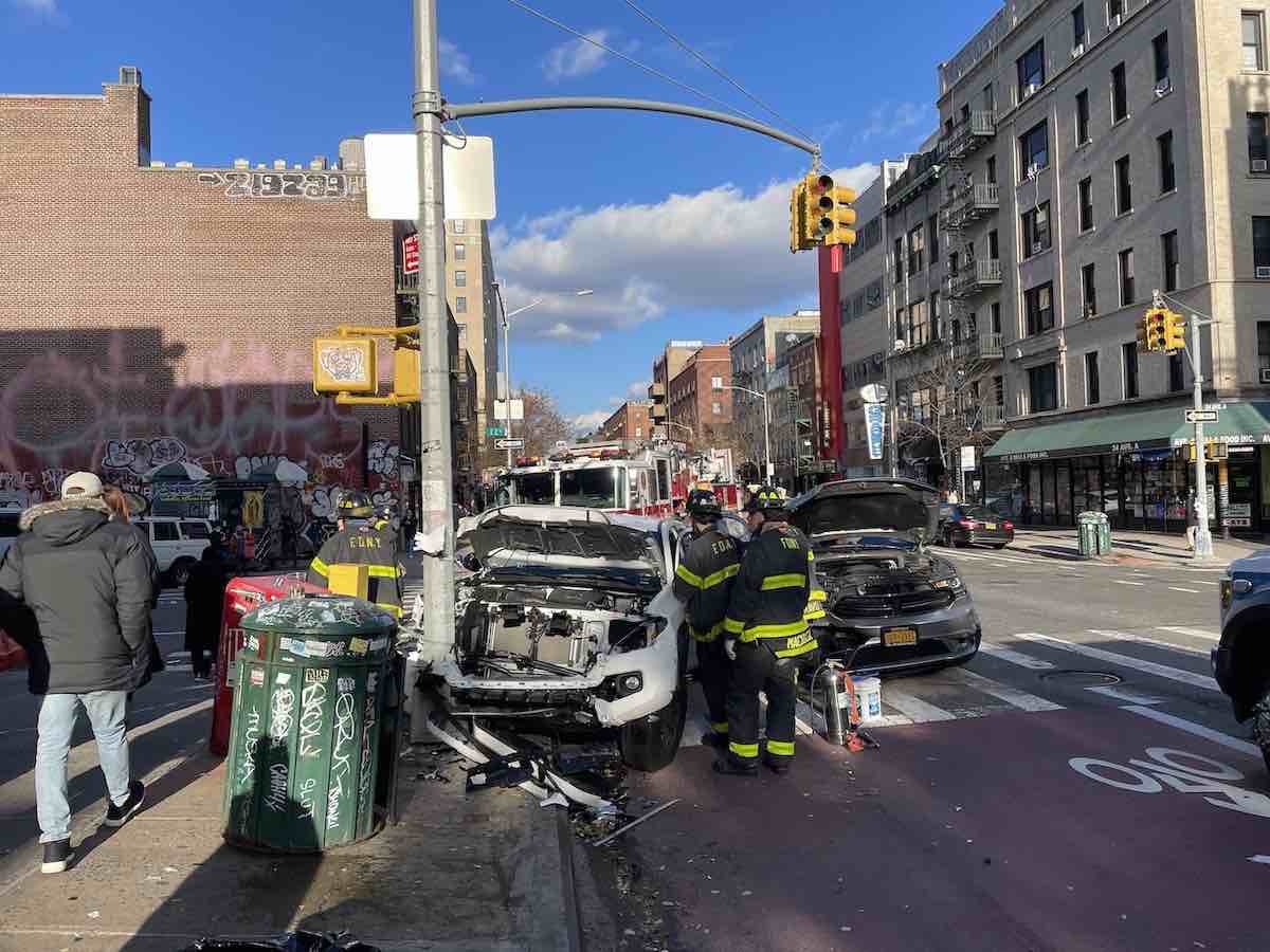 Two trucks crashed into a lightpole in Manhattan as FDNY members mill around.
