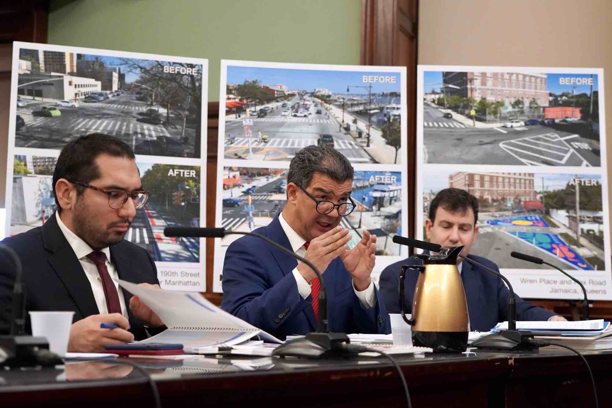 DOT Commissioner Ydanis Rodriguez gestures with his hands at a table in front of diagrams showing street improvements during a City Council hearing.