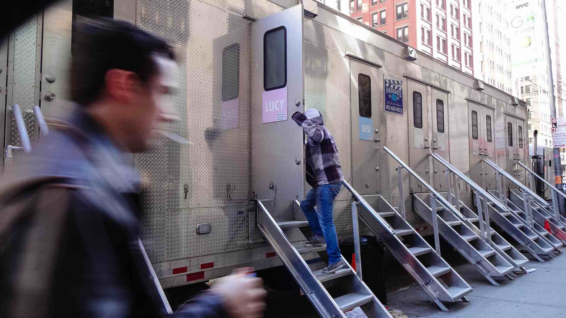 A staffer enters a silver movie trailer parked on a NYC block.