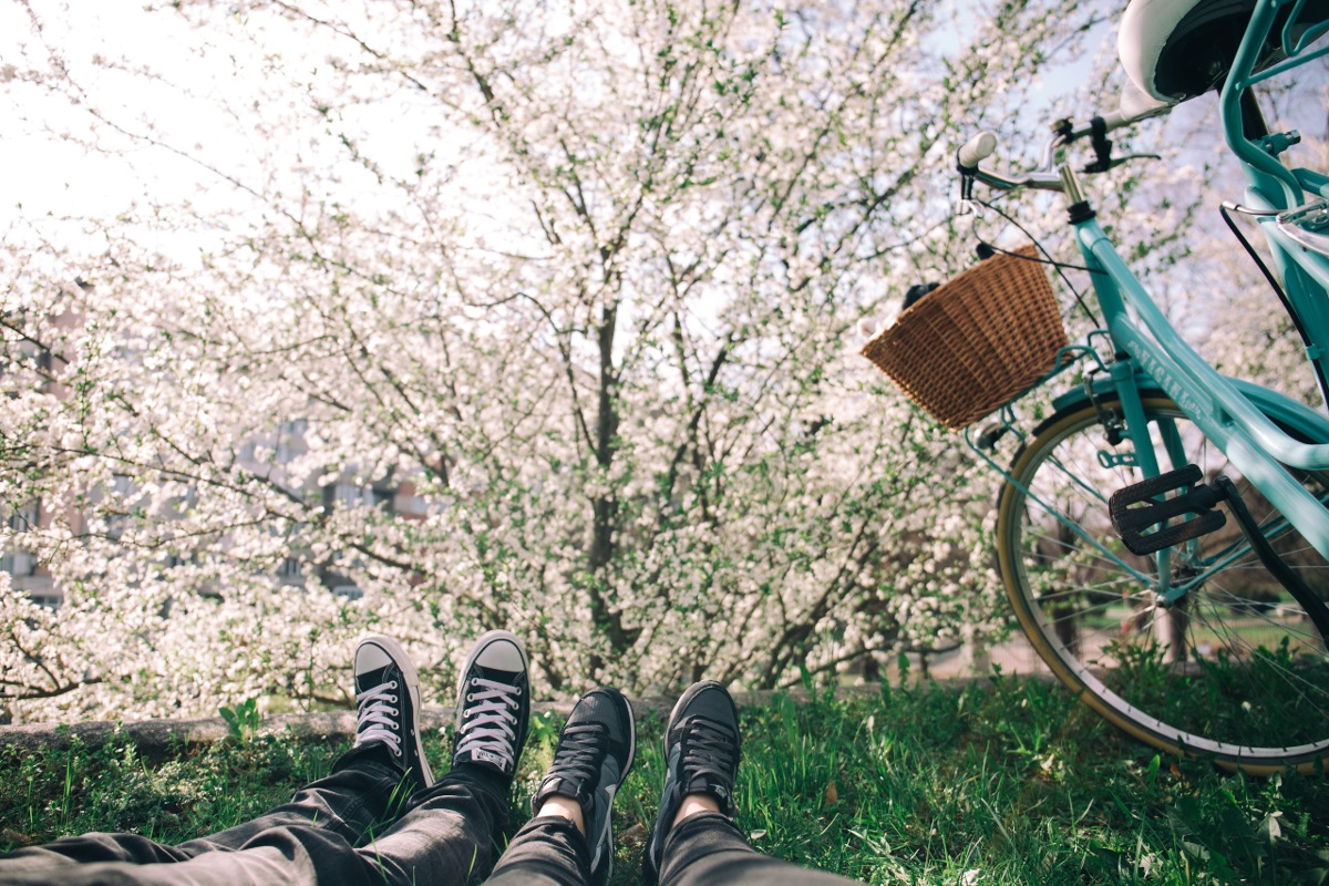 Two people lie on the grass next to a blue bicycle with a basket.
