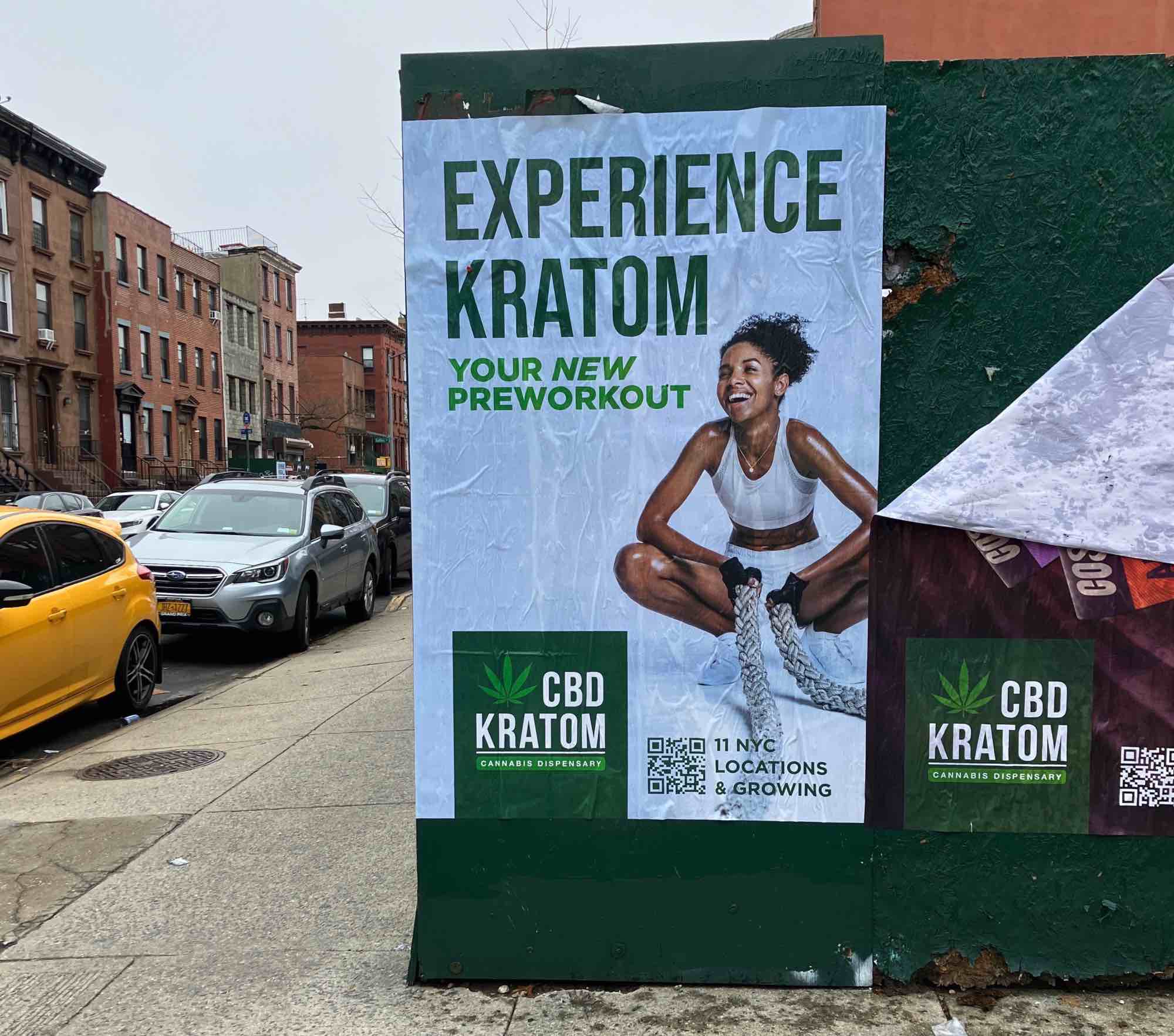 A wheatpaste ad for "CBD Kratom" as "Your new preworkout" with a woman in workout gear squatting next to the ad copy.