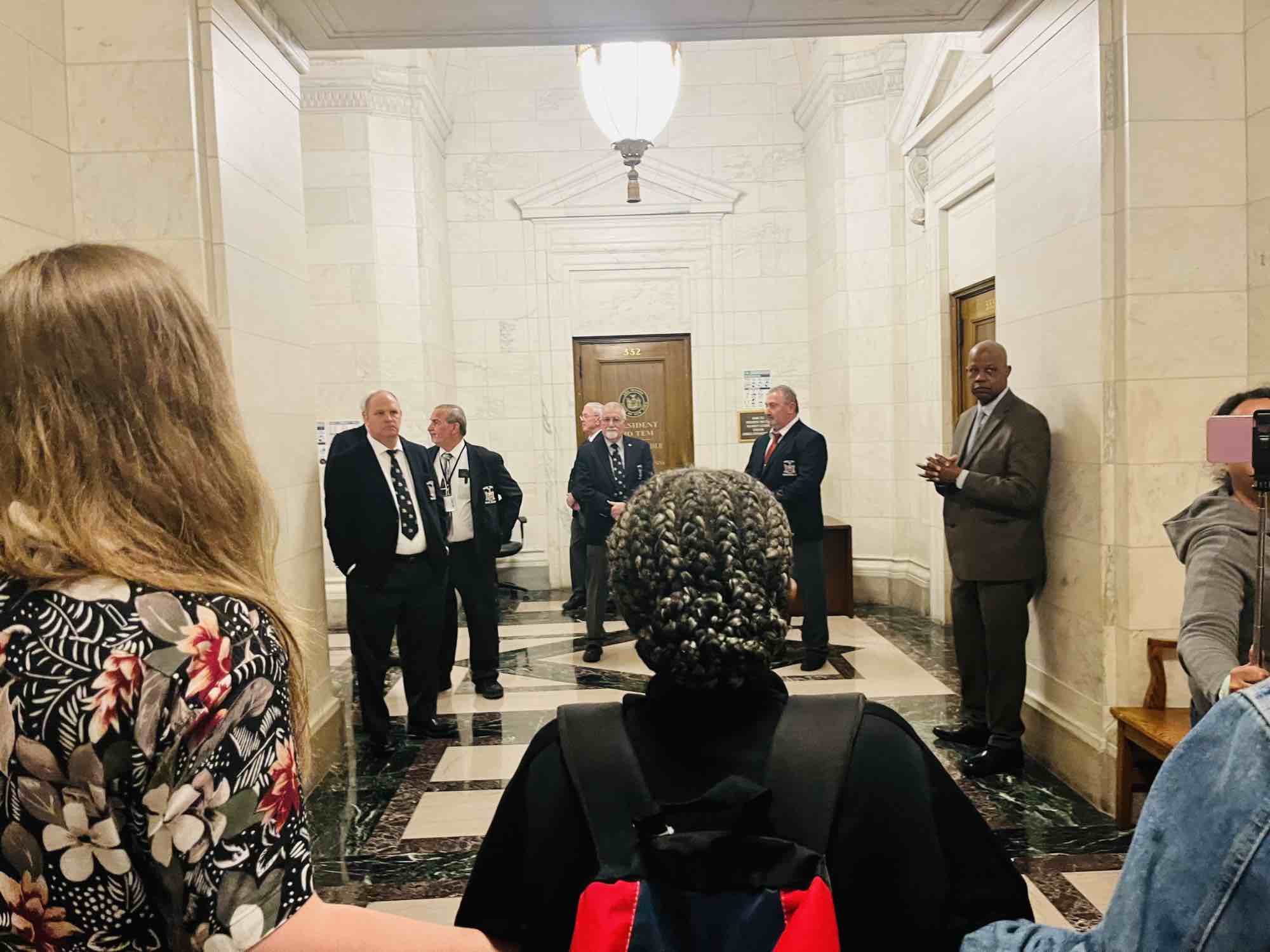 Men in ill-fitting suits stand around preventing housing activists from disrupting proceedings on the Senate site.