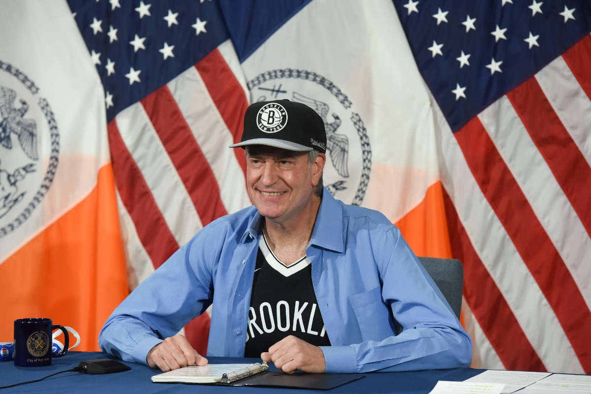 Then-Mayor Bill de Blasio wearing a Brooklyn Nets hat and jersey with a blue button-down.