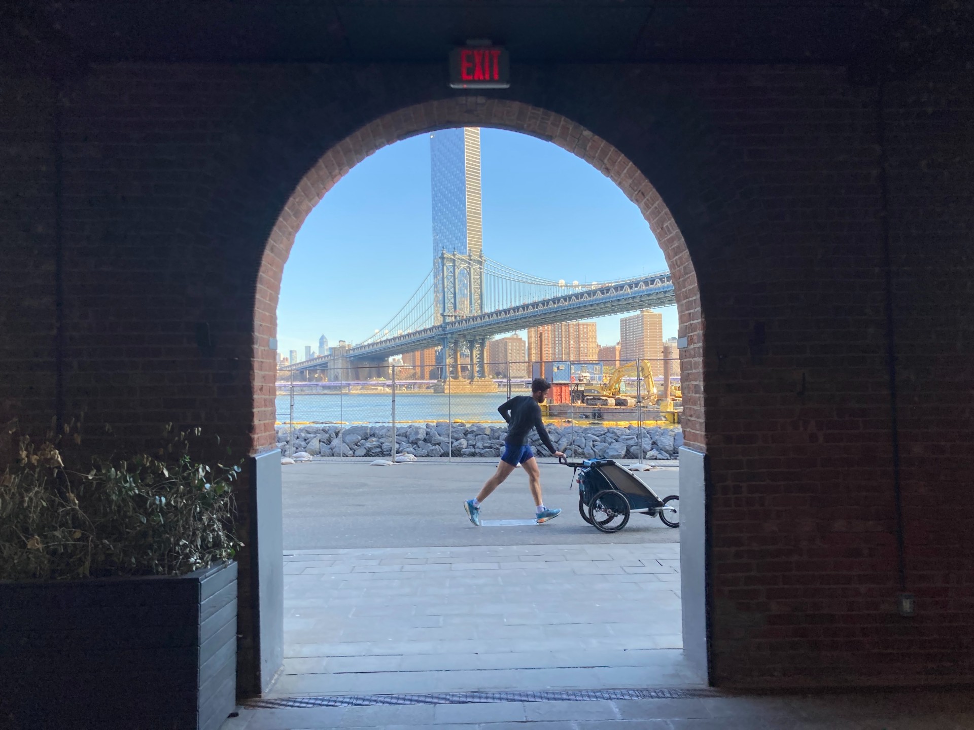 A man jogs with a baby carriage in front of the Brooklyn Bridge