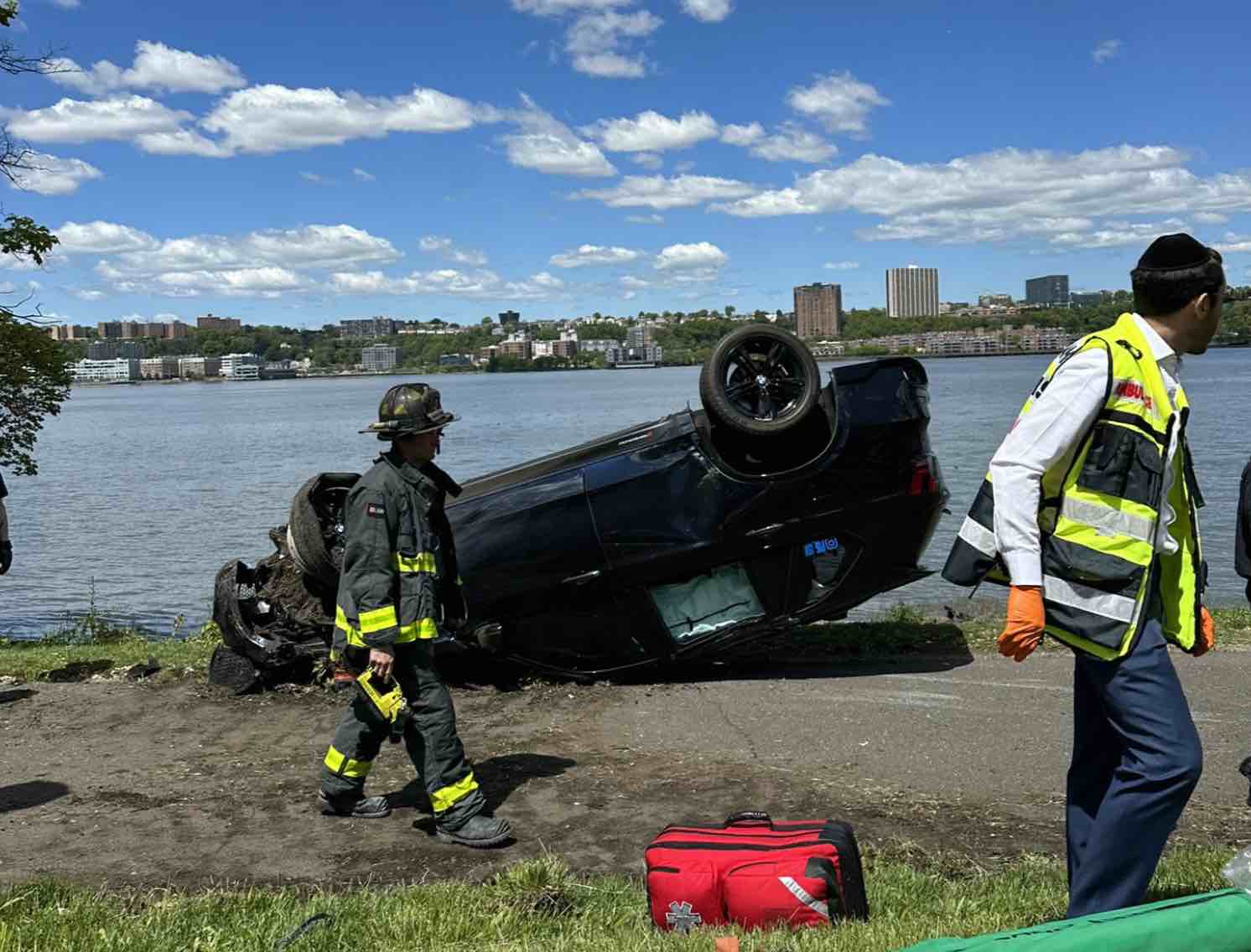 An SUV sits upside down in the bike path in Riverside Park, FDNY and EMS workers walk by.