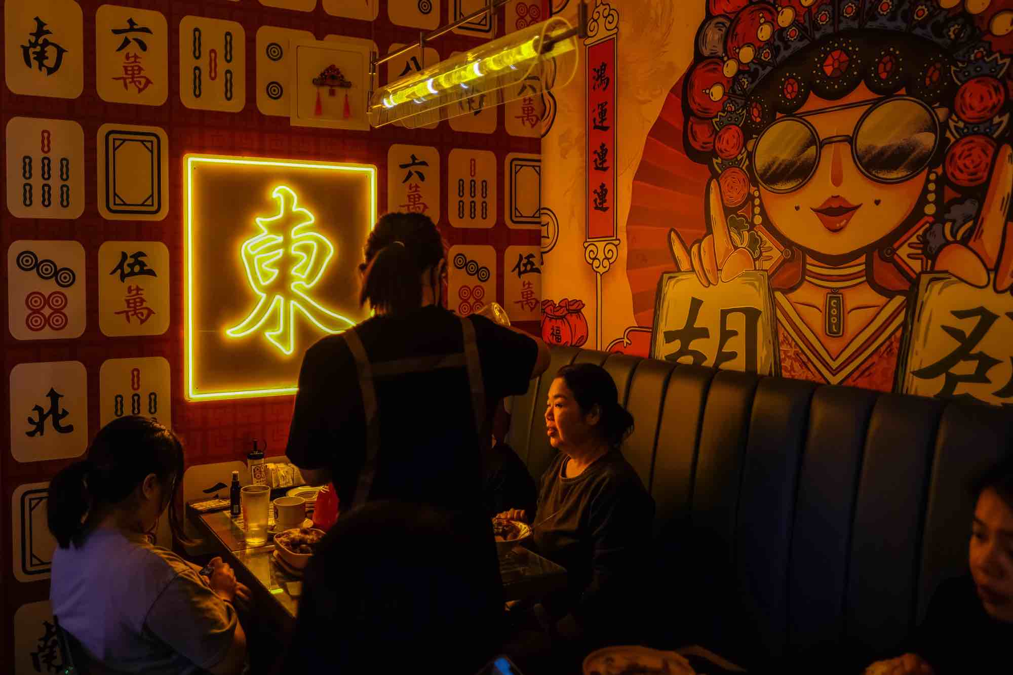 Two diners sit under a neon sign in a booth at Mabu Cafe.