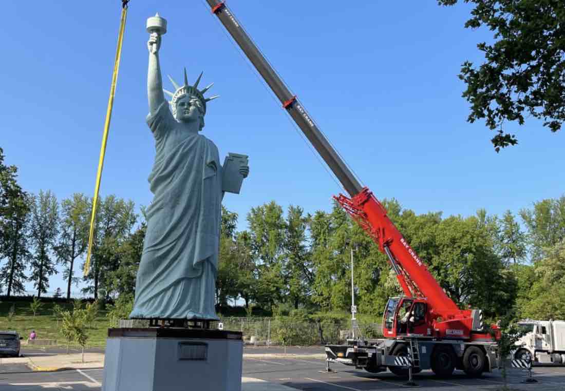 The Statue of Liberty replica being moved by crane in the Brooklyn Museum parking lot.