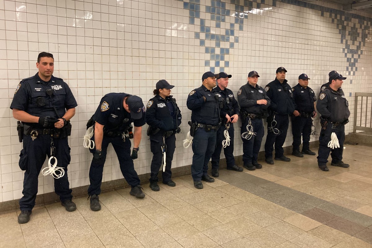 NYPD officers stand in a row in a subway station.