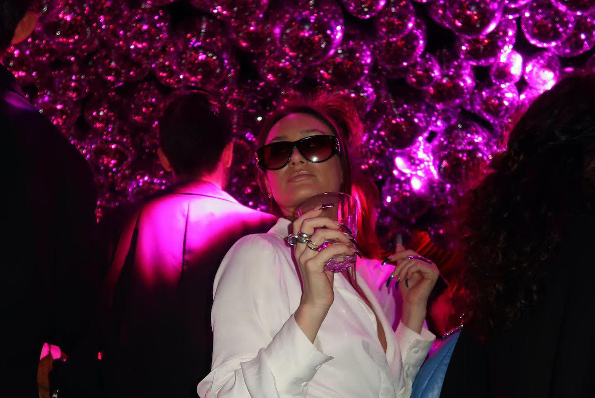 Melissa Rich, wearing sunglasses, poses in front of a large bunch of purple mylar balloons.