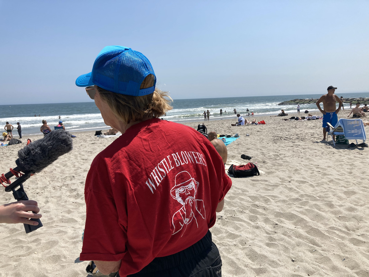 Rockaways lifeguard Janet Fash, in a red T-shirt and blue baseball cap, her back turned to the camera, at the beach.