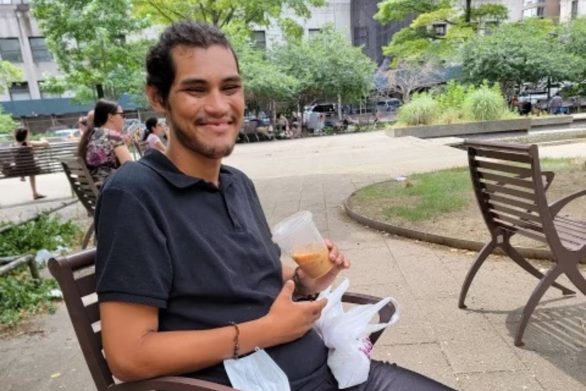 Joshua Valles sitting in a park smiling and drinking an iced coffee.